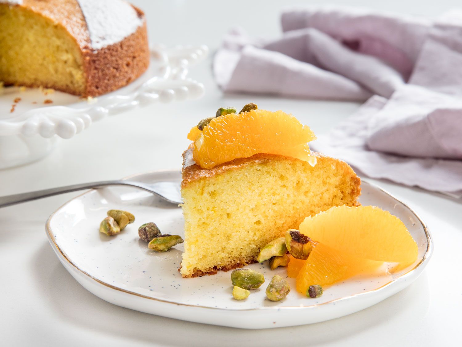 A slice of olive oil cake topped with orange segments and pistachios.