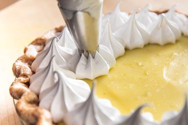 Piping whipped cream on top of a lemon meringue pie.