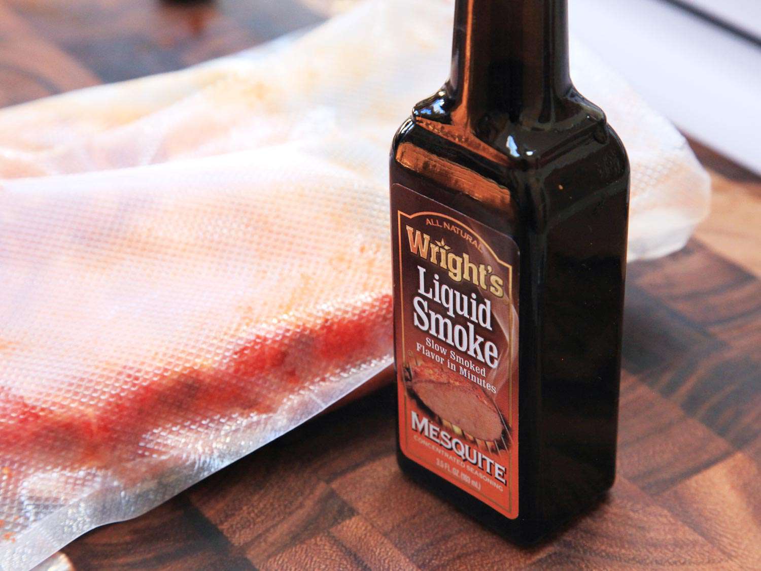 A bottle of Wright's liquid smoke next to a sous vide packet of meat.
