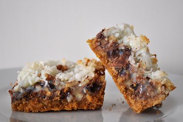 Two Hello Dolly bars with a graham cracker crust, chocolate chips, pecans, and toasted coconut on top.