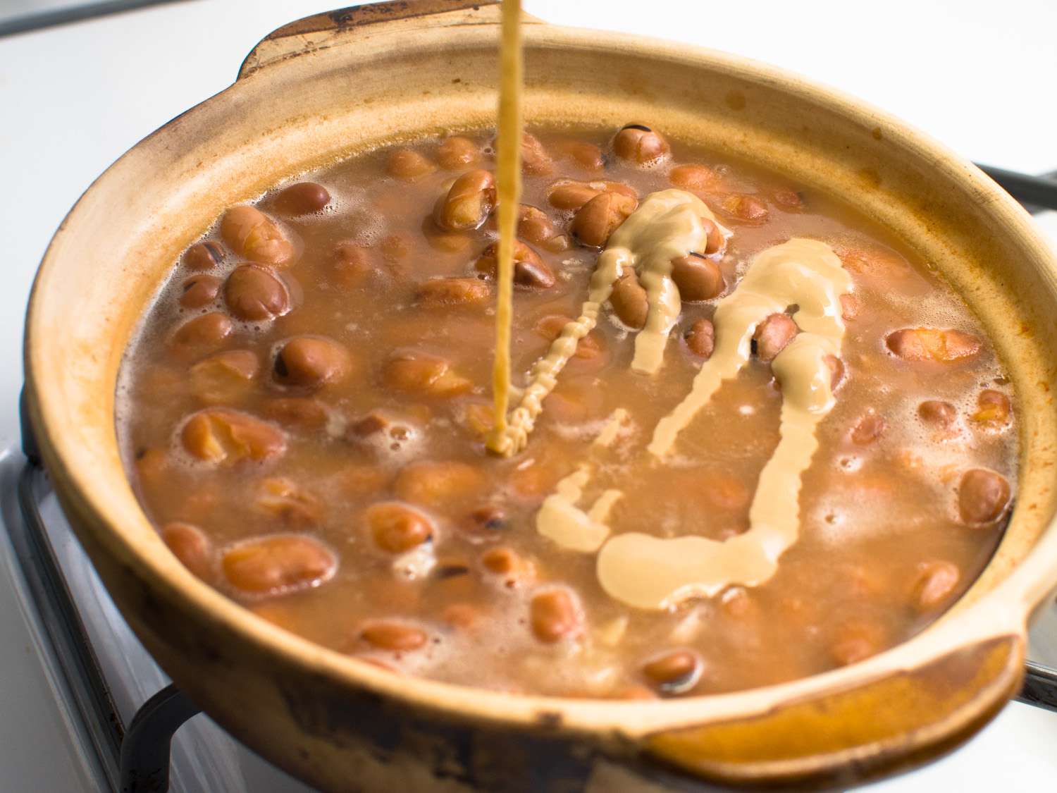 Tahini is added to a pot of simmering favas.