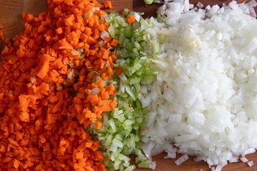 Ingredients for mirepoix; diced carrots, celery, and onions on a cutting board.