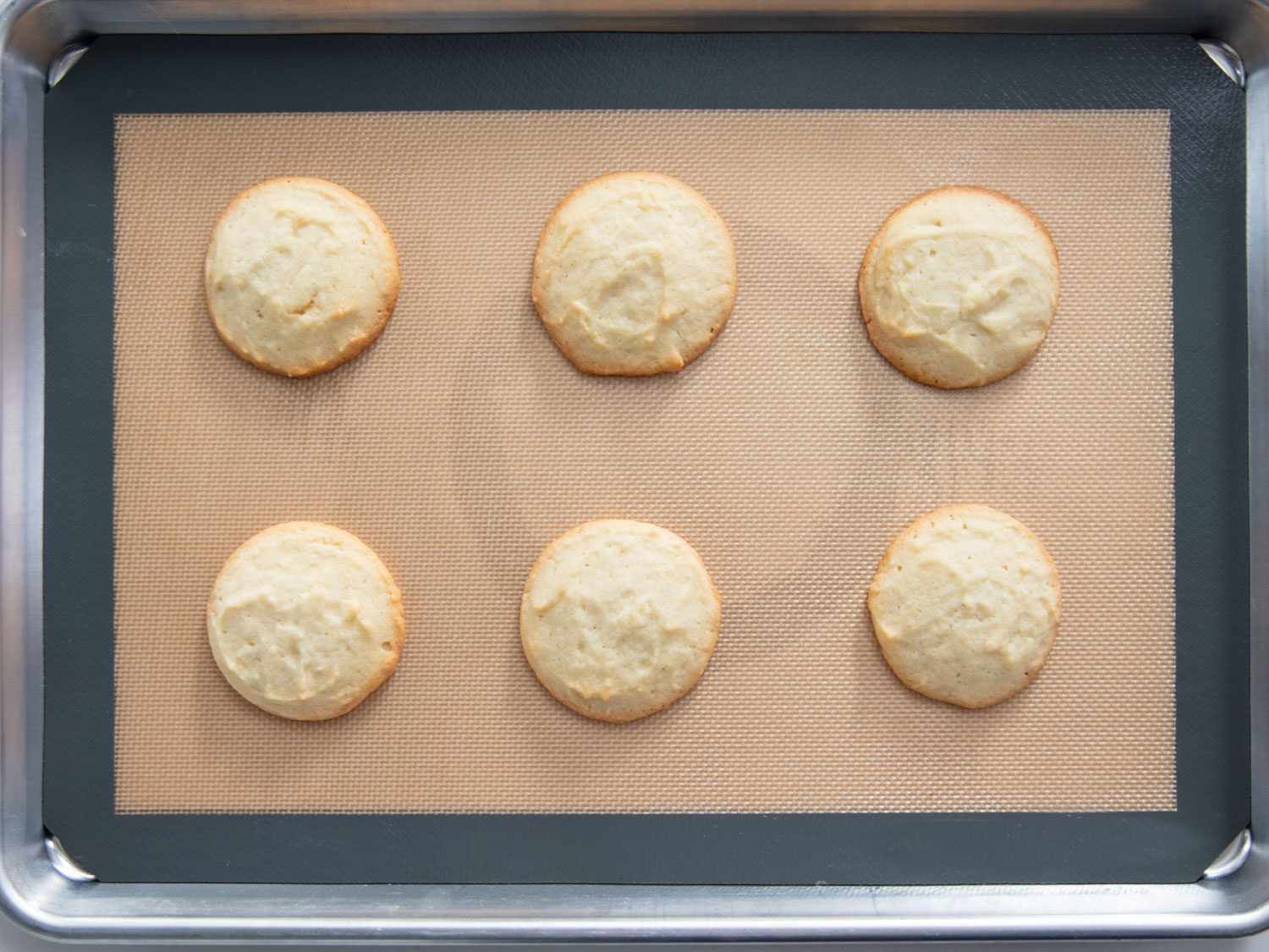 头顶上未加糖霜的lofhouse风格饼干，边缘泛黄，在硅胶衬里的烤盘上烘烤
