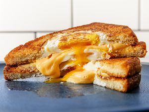 两半的烤奶酪洞鸡蛋三明治堆叠在一起，奶酪和鸡蛋从中间溢出。