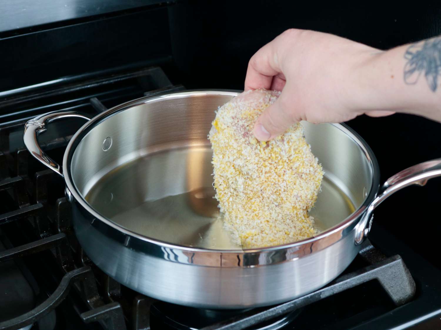 a chicken cutlet being lowered in cooking oil in a saute pan