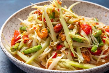 Side view of som tum thai (green papaya salad) in a serving bowl