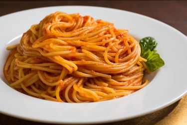 一个serving of spaghetti that has been lightly coated with tomato sauce and fashioned into a swirl-like heap in a shallow bowl.