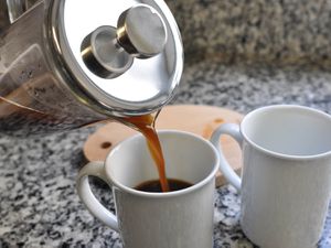 A French press pouring into two white coffee cups.