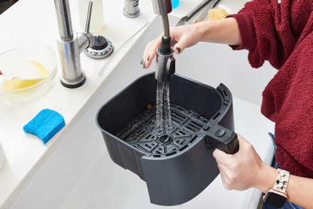 A person cleaning an air fryer basket in the sink