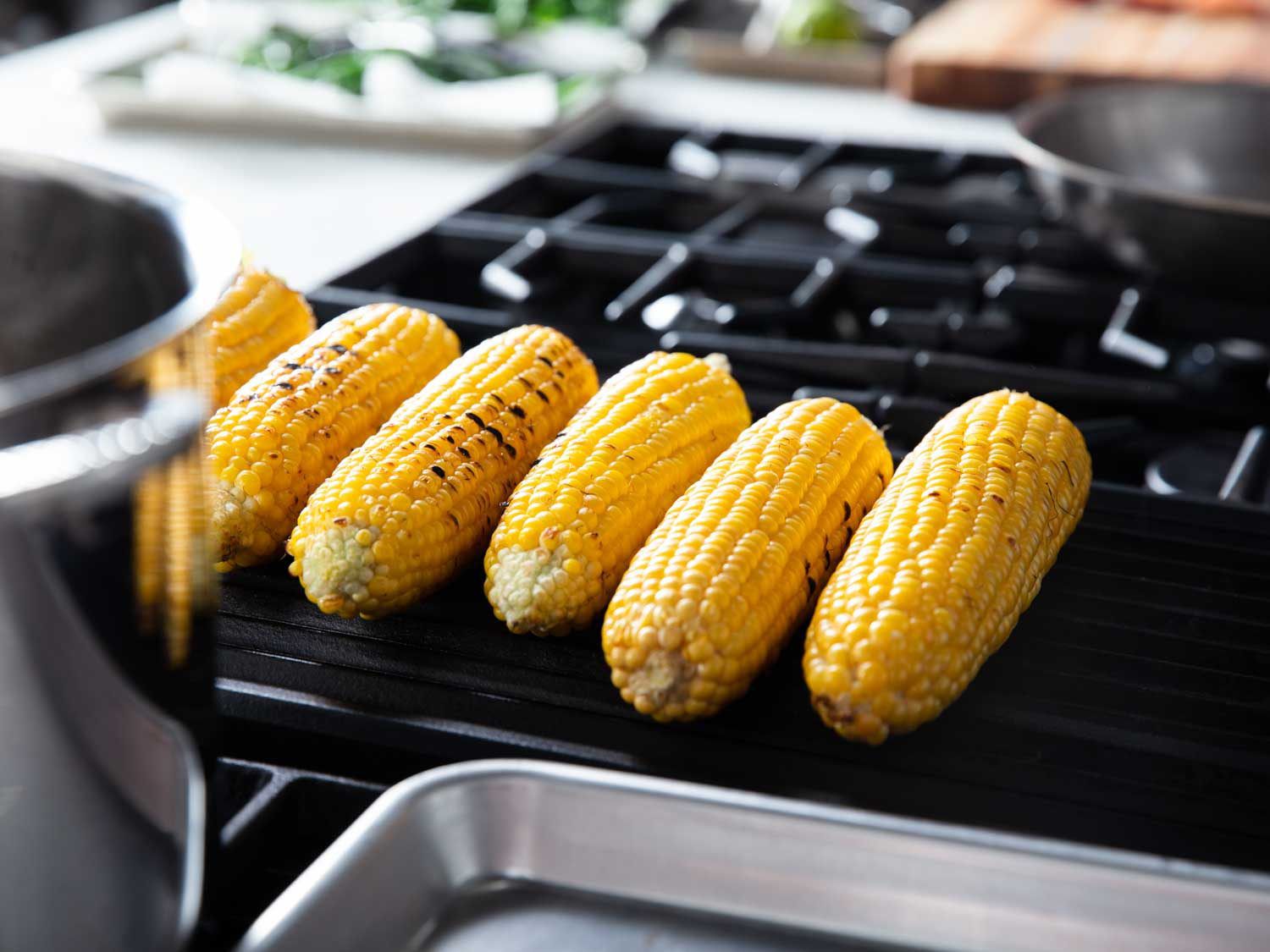 Ears of corn cooking on an indoor gas grill.