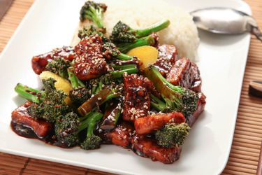 Crispy tofu in a sesame seed sauce with broccoli and a bed of rice on a white plate