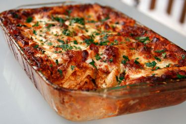 A rectangular glass baking pan of lasagna bolognese sprinkled with fresh chopped herbs.