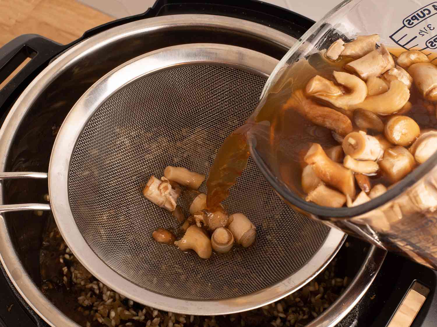 将蘑菇高汤通过细筛网倒入高压锅中，筛网将蘑菇的固体部分筛住。