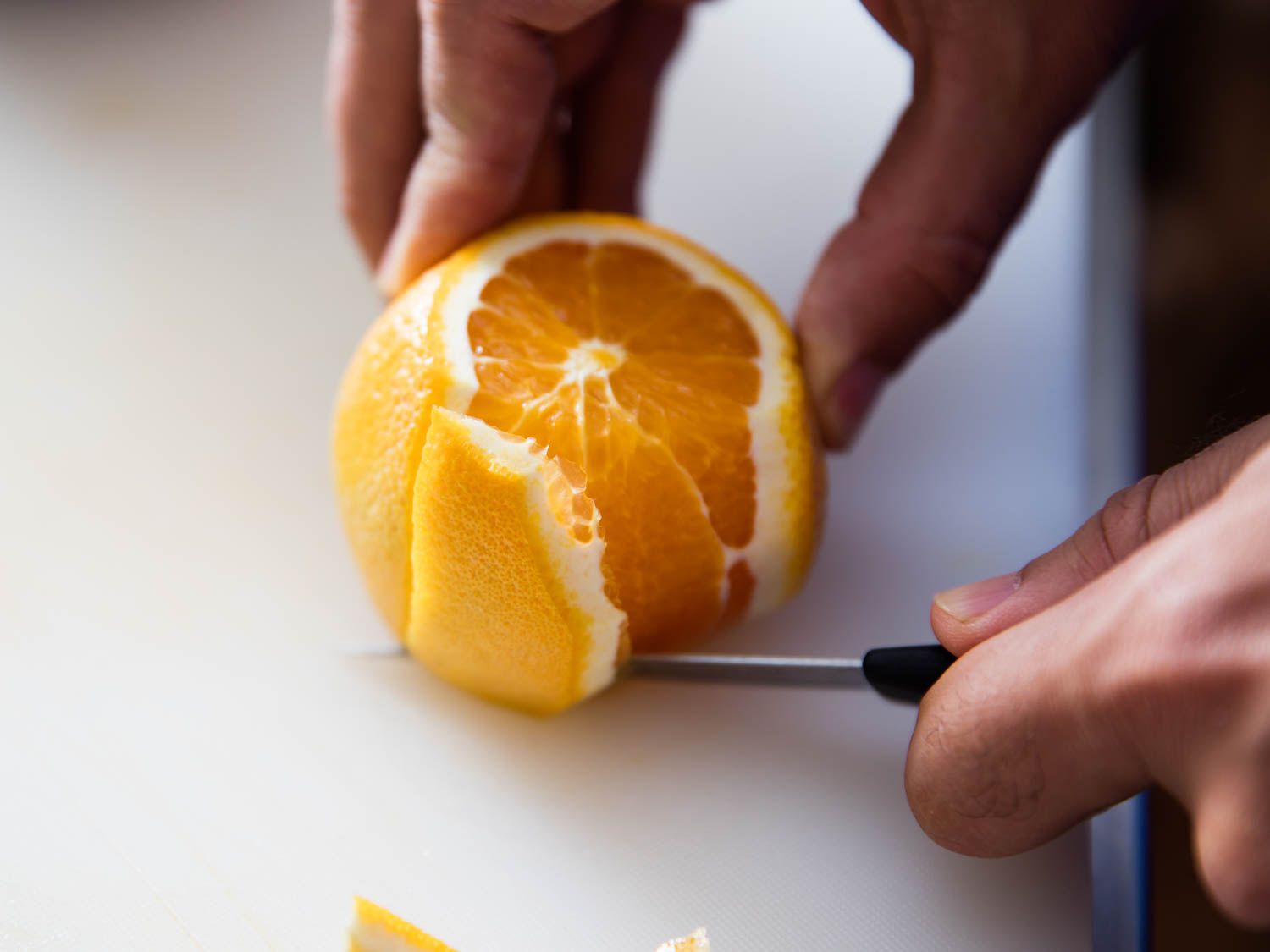 A pairing knife peeling an orange