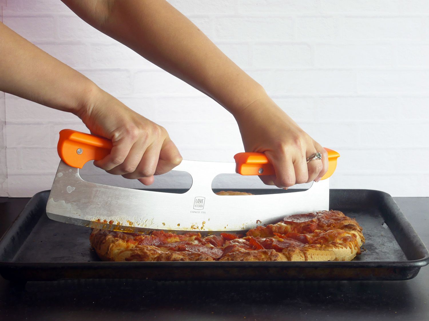 using the original pizza cutter to slice up a pepperoni pizza on a sheet tray