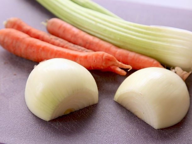 切成两半并去皮的洋葱放在砧板上。整根胡萝卜和芹菜落在后面。