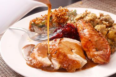 Gravy pouring over roast turkey plated with stuffing