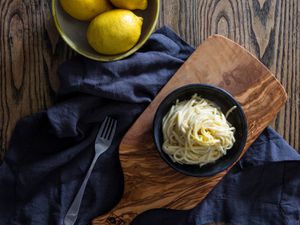 一碗柠檬面食放在橄榄木砧板上，配上深蓝色亚麻餐巾。