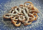 A single funnel cake on a blue platter, dusted with powdered sugar.