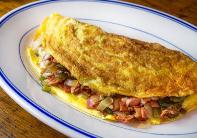 A Western omelette with bell peppers, onion, ham, and cheese on an oval plate.