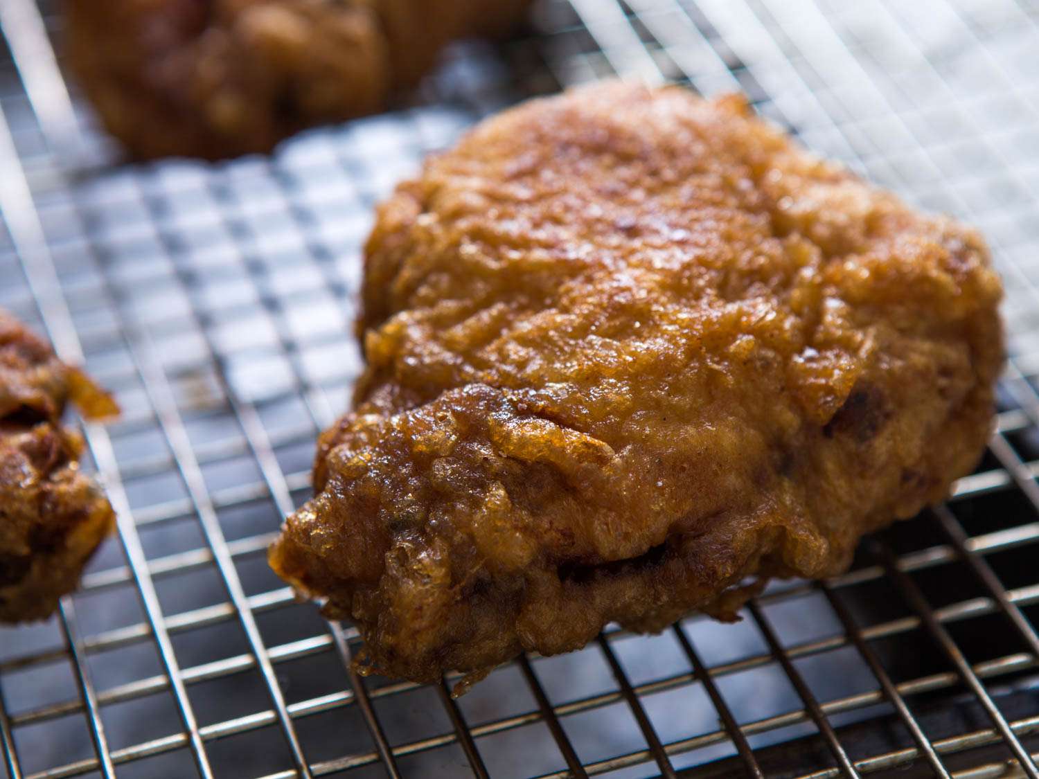 Fried chicken thigh resting on wire rack set over a baking sheet