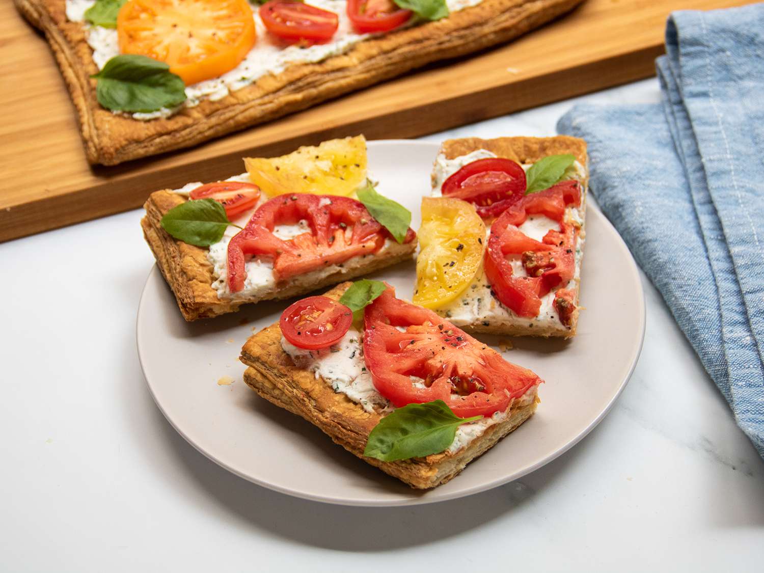 Slices of tomato tart on a plate, set in front of a cutting board with the rest of the tomato tart