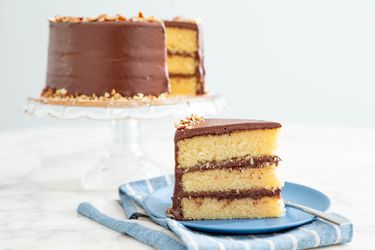 一块三层杏仁蛋糕，涂着黑巧克力糖霜，放在蓝色的盘子上，剩下的蛋糕放在白色的底座上