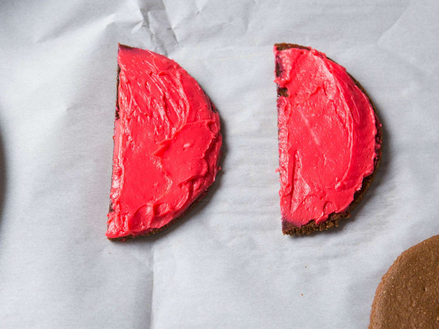 Two half disks of chocolate graham cookie frosted with red icing to the edges.