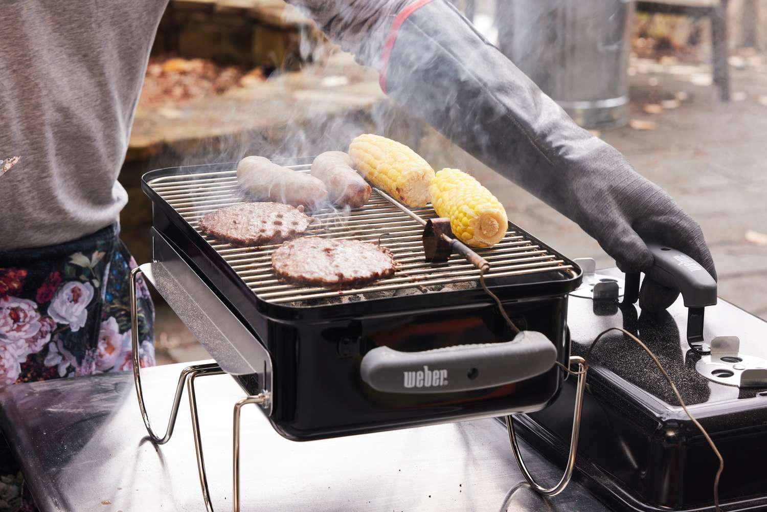 在便携式木炭烤架上烹饪汉堡、小鲜肉和玉米