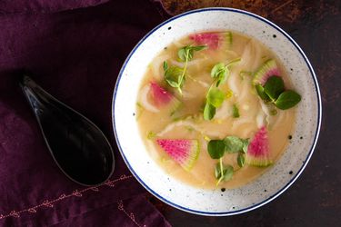 A bowl of miso soup topped with watermelon radish slices and greens.