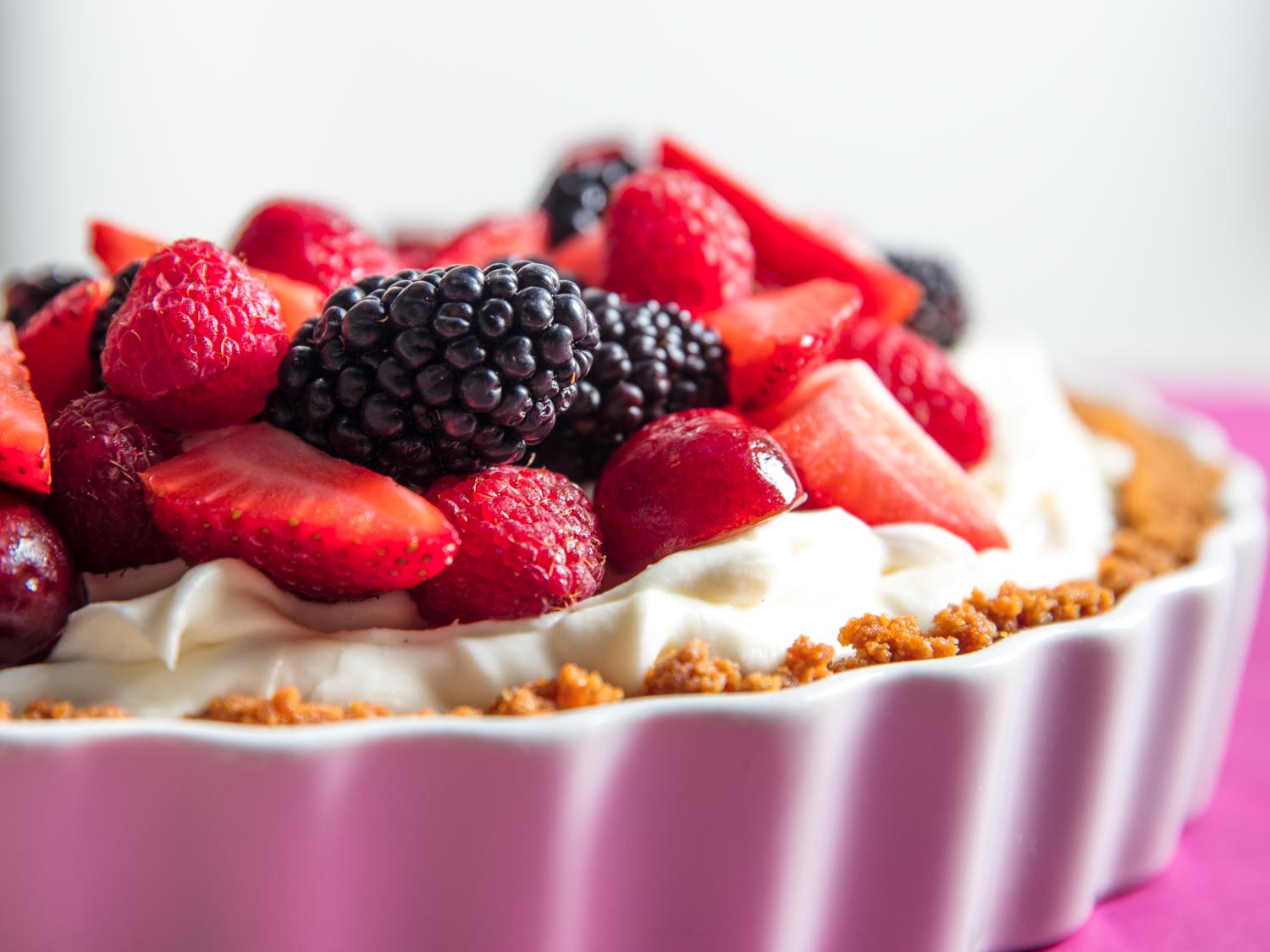 未烘焙的芝士蛋糕的特写，上面堆满了树莓、黑莓、一半的樱桃和一半的草莓。＂width=