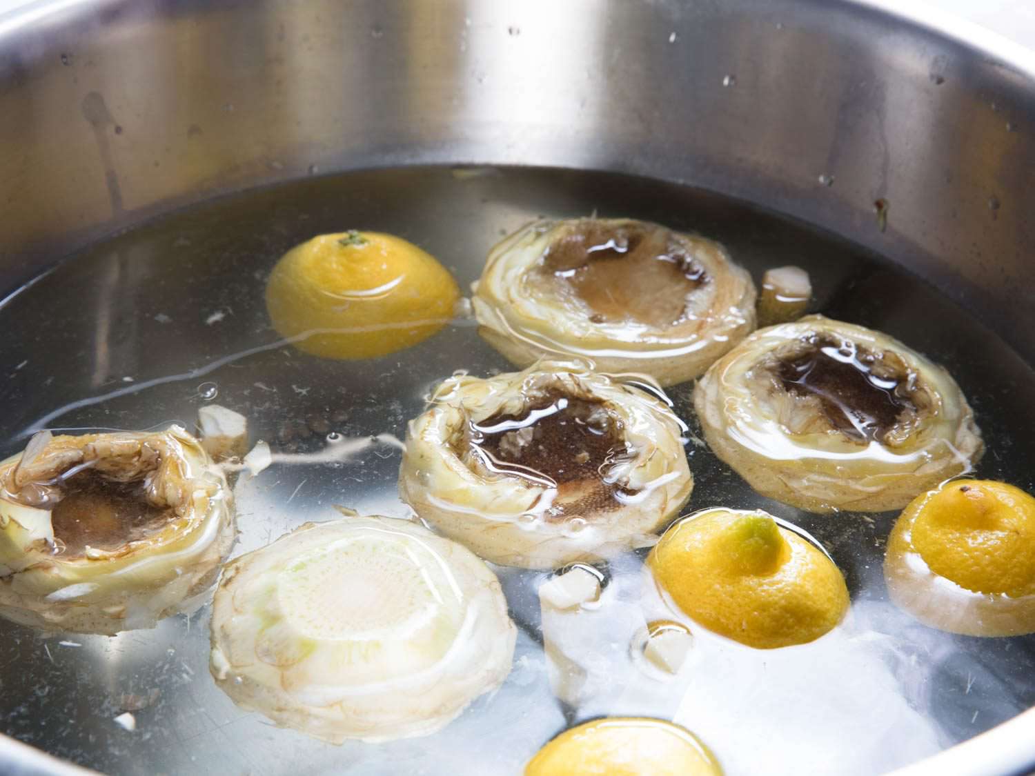 Cleaned artichoke hearts floating with lemon halves in a metal bowl of water