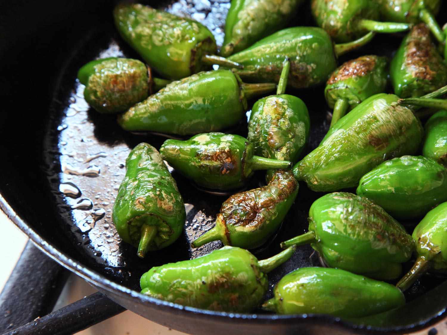 Padrón peppers charring in a cast iron skillet.