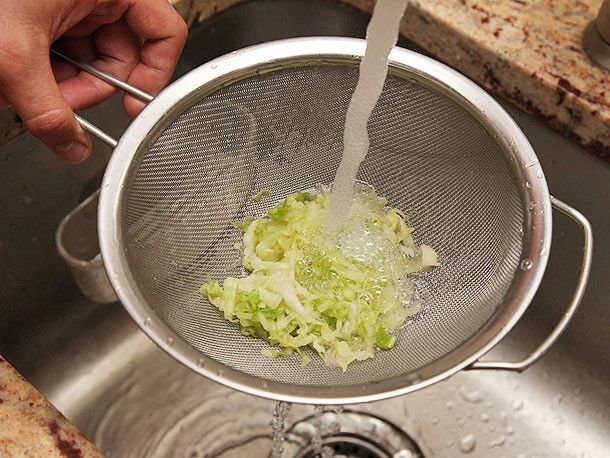 作者在水槽中用细网过滤器冲洗腌卷心菜丝。