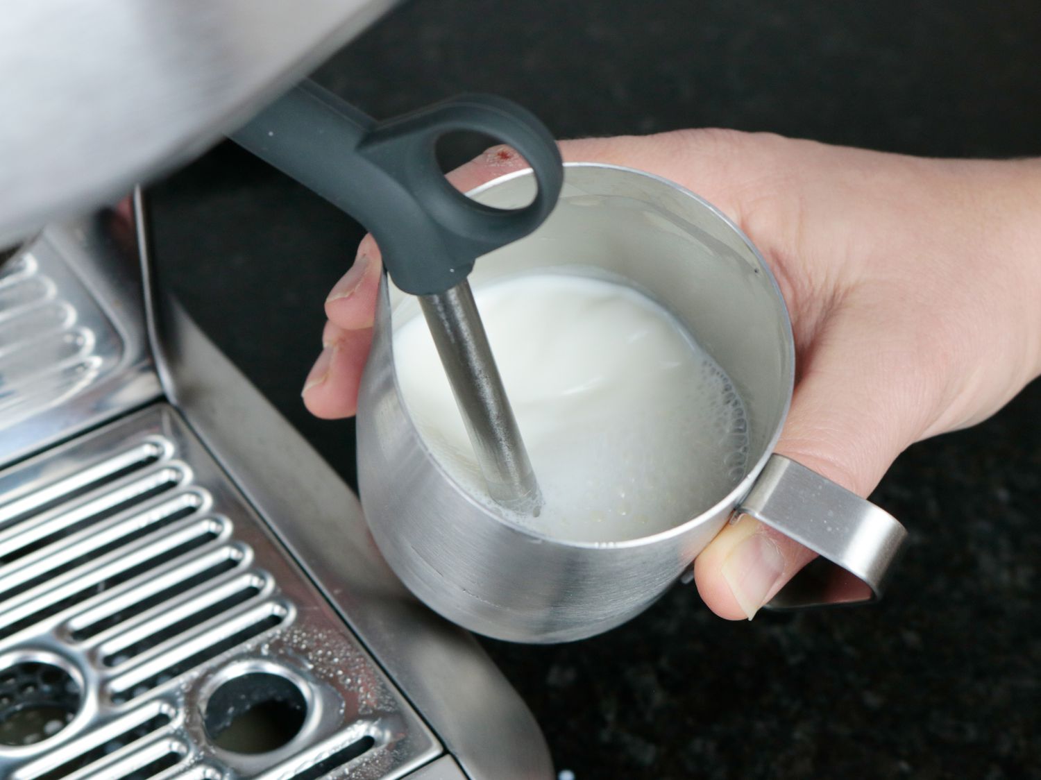 an espresso machine steam wand in a pitcher of milk