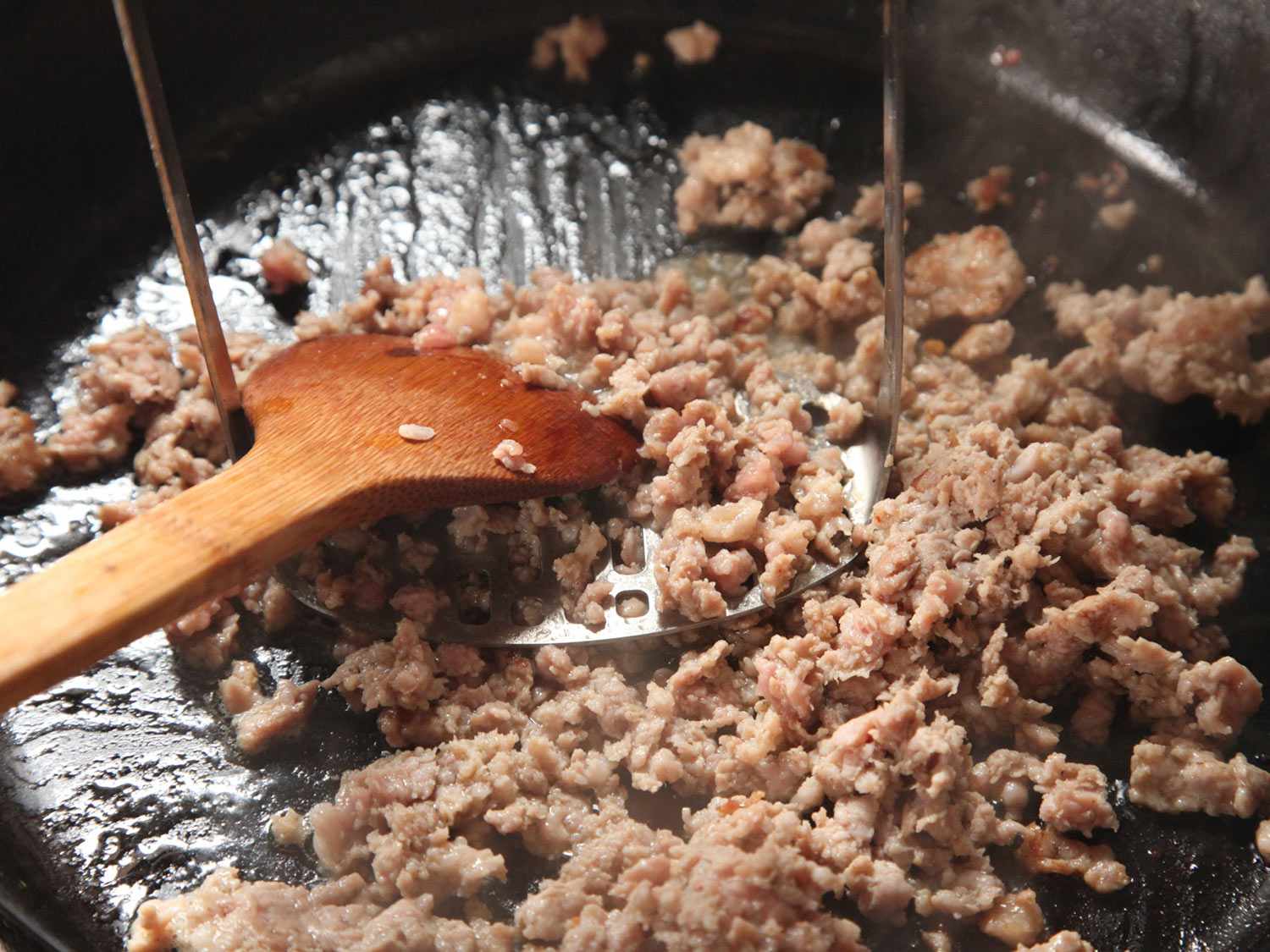 用木勺和金属土豆捣碎器在铸铁煎锅中打碎香肠gydF4y2Ba