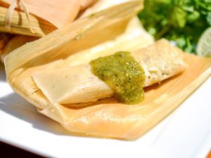 A tamale, unwrapped and still on its husk, with green salsa on top.