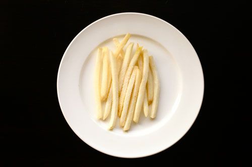 黑色背景的白色瓷盘里装着一些麦当劳的冷冻薯条。