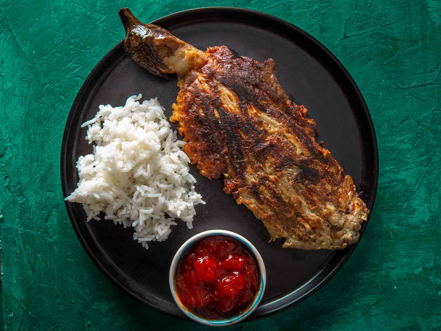 tortang talong on a black plate with white rice and banana ketchup