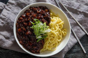 A bowl of jjajangmyeon with a thick and hearty black bean sauce on one side and fresh noodles on the other.