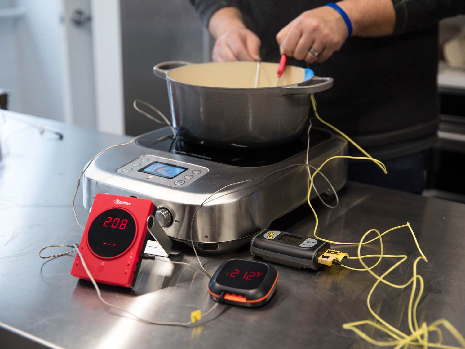 三种不同的温度计在感应燃烧器上检查荷兰烤箱中沸水的温度