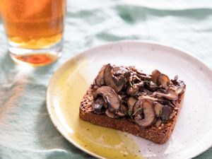 A slice of Danish rye bread toast topped with sautéed mushrooms, next to a glass of beer
