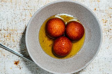 Three golden brown gulab jamuns soaking in syrup in a grey bowl