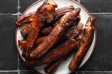 Roasted Chinese spare ribs on a ceramic plate on a black tile background.