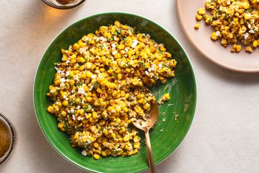 Esquites in a green ceramic bowl with a serving spoon