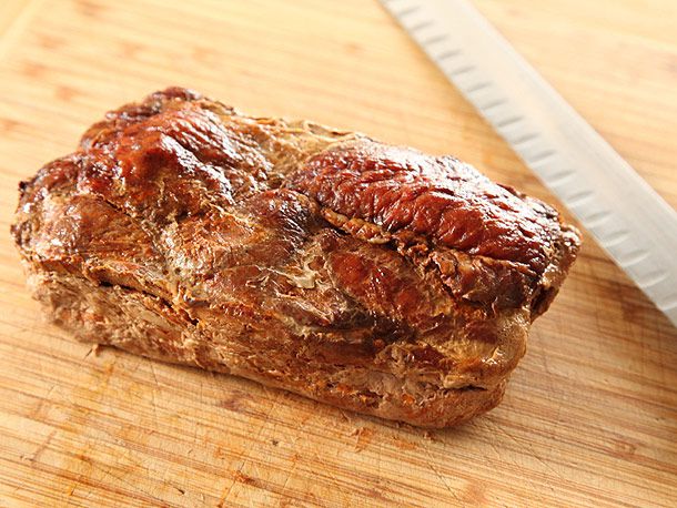 烤过的al pastor肉放在砧板上，旁边是一把刀。