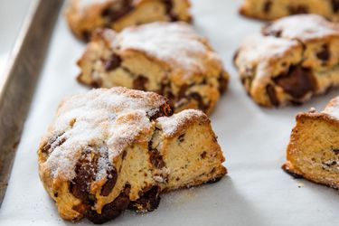 Wedge-shaped chocolate chunk scones on parchment-covered baking sheet.