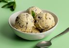 A white porcelain bowl holding three scoops of mint chocolate chip ice cream.