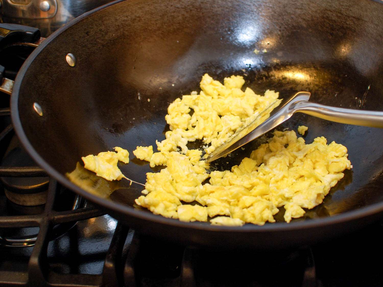 A metal spatula stirring scrambled eggs in a wok.