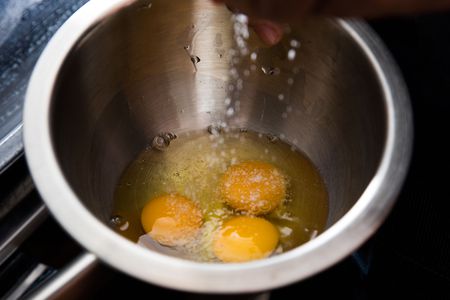 salt being sprinkled into a bowl with raw eggs before whisking